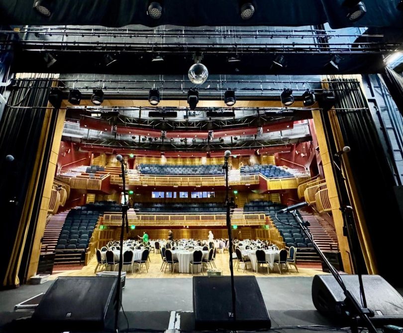 View from the Millennium Forum stage looking out into the auditorium, with microphones in the foreground and round tables set up on the main floor for a formal event.