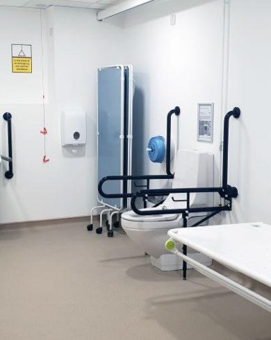 Accessible Changing Places facility with height-adjustable bench, support rails, accessible toilet and sink, and ceiling track hoist at the Millennium Forum.