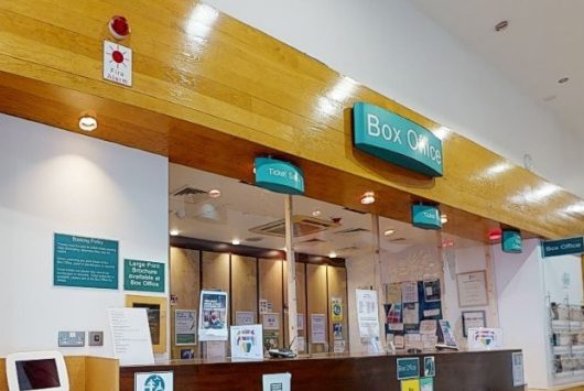 Millennium Forum Box Office with glass service windows, teal signage, and customer information displays on the counter and walls.