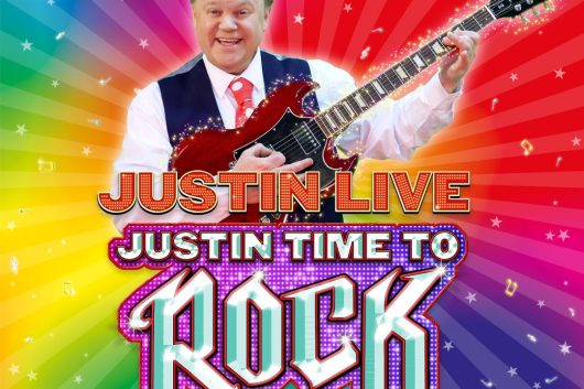 Colourful promotional image for Justin Live: Just In Time To Rock. Children’s entertainer Justin Fletcher is shown smiling and holding an electric guitar, dressed in a white shirt and waistcoat. The background bursts with rainbow colours and sparkles, creating a fun, high-energy vibe. Bold, glittery text in red, pink, and purple reads: “JUSTIN LIVE – JUST IN TIME TO ROCK”. Logos for “Something Special” and “Justin Fletcher” appear in the corners, signalling a family-friendly live show full of music and fun.