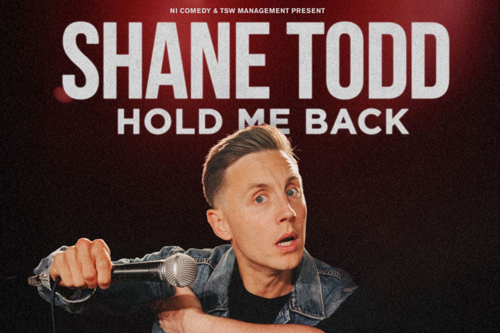 Promotional poster for comedian Shane Todd’s show Hold Me Back. Shane is pictured front and centre in a leather jacket, gripping a microphone stand with a surprised or defensive expression, adding a humorous edge. The background is a dark red-to-black gradient, with bold white text displaying his name and the show title above. The design is punchy and dynamic, reflecting Shane Todd’s energetic stand-up style.